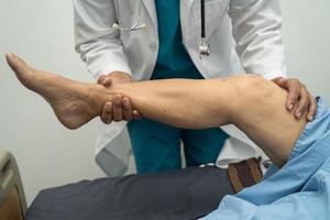 medico asiatico fisioterapista che esamina, massaggia e tratta il ginocchio e la gamba del paziente anziano nell'ospedale dell'infermiera della clinica medica ortopedica. foto