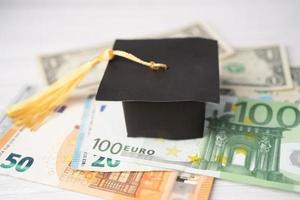 cappello di divario di laurea su banconote in euro e dollari americani, concetto di insegnamento della tassa di studio dell'istruzione. foto