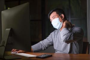 uomo che indossa una maschera preventiva e lavora da casa di notte in situazione di malattia da virus corona. lavoro da casa e concetto sano foto