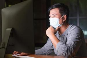 uomo che indossa una maschera preventiva e lavora da casa di notte in situazione di malattia da virus corona. lavoro da casa e concetto sano foto