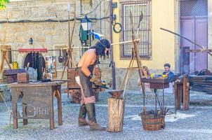 Guimaraes, Portogallo - 24 giugno 2017 fabbro uomo che forgia ferro metallo in piazza di ciottoli con case ed edifici medievali foto