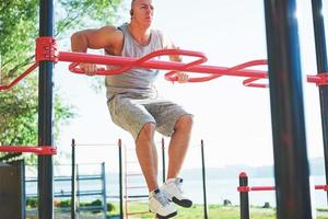 uomo muscoloso con bel torso che si esercita su barre orizzontali su uno sfondo sfocato del parco. giovane che fa pull-up all'aperto foto