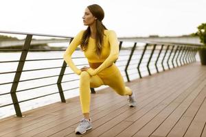 giovane donna che fa esercizio di stretching sul molo lungo il fiume foto