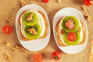 toast con kiwi, formaggio, noci e pomodorini su un pezzo di tela di sacco con noci e pomodorini intorno. vista dall'alto foto