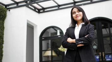 donna d'affari asiatica sorridente e in piedi davanti all'ufficio foto