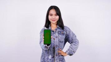 donne asiatiche sorridenti che indossano una giacca di jeans e tengono un telefono con schermo verde con sfondo bianco isolato foto