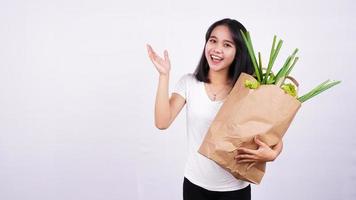 bella donna asiatica che tiene sacchetto di carta di verdure fresche molto felice che punta con la mano e il dito su sfondo bianco isolato foto