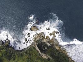 vista aerea dall'alto verso il basso delle onde oceaniche giganti che si infrangono e si schiumeggiano nella spiaggia di corallo foto