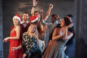 festa con gli amici. amano il natale. gruppo di giovani allegri che trasportano stelle filanti e flauti di champagne che ballano alla festa di capodanno e sembrano felici. concetti sullo stile di vita insieme foto