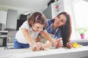 famiglia felice in cucina. concetto di cibo per le vacanze. madre e figlia che preparano l'impasto, cuociono i biscotti. famiglia felice nel fare i biscotti a casa. cibo fatto in casa e piccolo aiutante foto