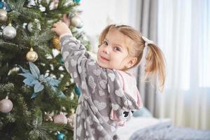 buon natale e buone feste. giovane ragazza che aiuta a decorare l'albero di natale, tenendo in mano alcune palline di Natale foto