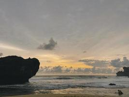 tramonto nel mare tra onde e rocce in indonesia foto