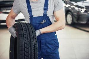 meccanico che tiene un pneumatico al garage di riparazione. sostituzione gomme invernali ed estive foto