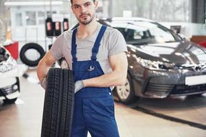 meccanico che tiene un pneumatico al garage di riparazione. sostituzione gomme invernali ed estive foto