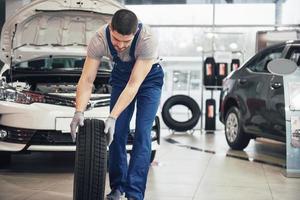 meccanico che tiene un pneumatico al garage di riparazione. sostituzione gomme invernali ed estive foto