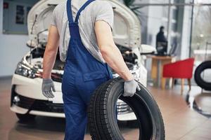 meccanico che tiene un pneumatico al garage di riparazione. sostituzione gomme invernali ed estive foto