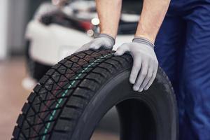 primo piano delle mani del meccanico che spingono un pneumatico nero in officina foto