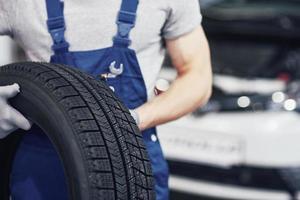 meccanico che tiene un pneumatico al garage di riparazione. sostituzione gomme invernali ed estive foto