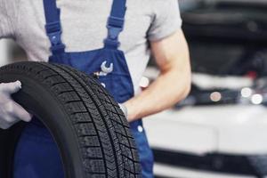 meccanico che tiene un pneumatico al garage di riparazione. sostituzione gomme invernali ed estive foto