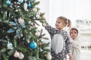 buon natale e buone feste. ragazze che aiutano a decorare l'albero di Natale, tenendo in mano alcune palline di Natale foto