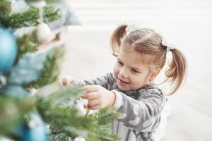 buon natale e buone feste. giovane ragazza che aiuta a decorare l'albero di natale, tenendo in mano alcune palline di Natale foto