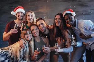 raggruppare bei giovani che fanno selfie nella festa di capodanno, migliori amici ragazze e ragazzi che si divertono insieme, posando persone con uno stile di vita emotivo. cappelli di Babbo Natale e bicchieri di champagne nelle loro mani foto