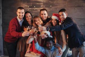 il nuovo anno sta arrivando. gruppo di allegri giovani multietnici in cappelli di Babbo Natale alla festa, in posa concetto di persone con uno stile di vita emotivo foto