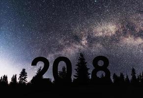 felice per il nuovo anno 2018 sfondo della Via Lattea su una stella luminosa tonalità del cielo scuro su sagome di pini foto