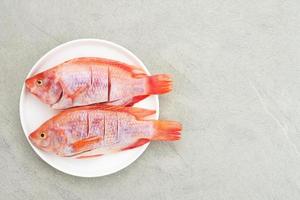 il pesce crudo di tilapia rossa è una specie di pesce d'acqua dolce, servito su un piatto bianco con spezie e limone. messa a fuoco selezionata foto