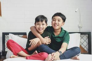 due fratelli asiatici felici che si siedono e che sorridono insieme sul letto foto