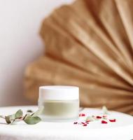 maschera cosmetica in polvere. vasetto di vetro con matcha su fondo bianco con petali secchi. foto