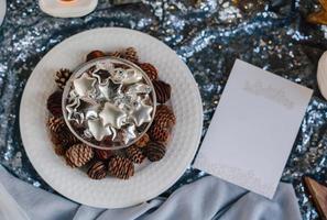 stelle d'argento di vetro in un vaso di vetro. giocattoli dell'albero di natale in un bicchiere su uno sfondo di tessuto lucido e pigne. copia spazio. foto