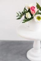 bouquet primaverile in vaso bianco su supporto bianco in legno. rose, tulipani e lisianthus. foto