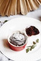 muffin al cioccolato in tazze rosse. piccolo ramekin in ceramica smaltata con torte marroni su sfondo grigio e bianco. foto