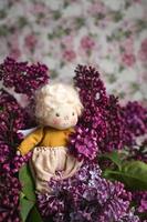 piccolo angelo dai capelli dorati nei fiori lilla blu, rosa, viola, viola. giocattolo fatto a mano nei colori viola lilla. biglietto d'auguri. foto