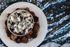 stelle d'argento di vetro in un vaso di vetro. giocattoli dell'albero di natale in un bicchiere su uno sfondo di tessuto lucido e pigne. copia spazio. foto