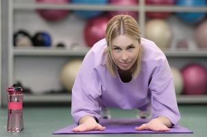 donna che fa esercizio di plancia su stuoie di yoga in palestra, vista frontale, donna che guarda l'obbiettivo. persone reali nel fitness club foto