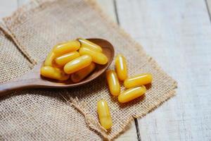 medicina capsula gialla o alimento supplementare dalla natura per la salute - capsule di pappa reale in cucchiaio di legno e fondo del sacco