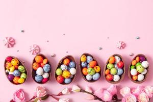 uova di pasqua di cioccolato e decorazioni piatte per bambini concetto di uova di caccia di pasqua su sfondo rosa. dolci a forma di uovo foto