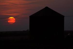 sole che tramonta dietro un granaio di metallo nel saskatchewan foto