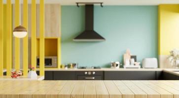 tavolo in legno vuoto e cucina sfocata sullo sfondo giallo della parete, piano in legno sul bancone della cucina sfocato.