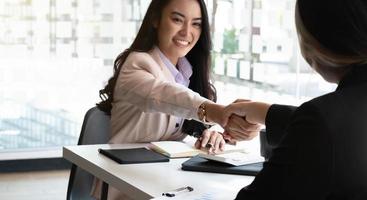 sorridente giovane imprenditrice asiatica stringe la mano felice incontro negoziazioni successo con carte millimetrate poste in ufficio. foto