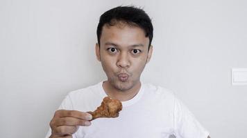 giovane uomo asiatico sta mangiando pollo fritto indossare camicia bianca foto