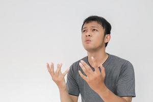 giovane uomo asiatico in maglietta grigia che prega con la faccia triste foto