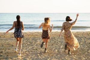amiche in abiti estivi che corrono verso il mare agitato foto