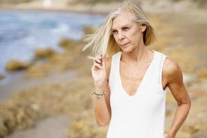 donna matura che cammina sulla spiaggia. donna anziana in piedi in una località balneare foto