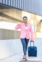 donna nera che cammina con una borsa da viaggio che indossa una giacca rosa. foto