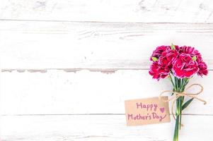 Fotografia concettuale per la festa della mamma - bellissimi garofani con carta modello isolata su un tavolo di legno luminoso, spazio per la copia, distesi, vista dall'alto, mock up foto