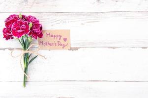 Fotografia concettuale per la festa della mamma - bellissimi garofani con carta modello isolata su un tavolo di legno luminoso, spazio per la copia, distesi, vista dall'alto, mock up foto