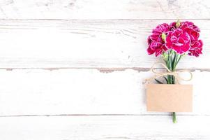 Fotografia concettuale per la festa della mamma - bellissimi garofani con carta modello isolata su un tavolo di legno luminoso, spazio per la copia, distesi, vista dall'alto, mock up foto